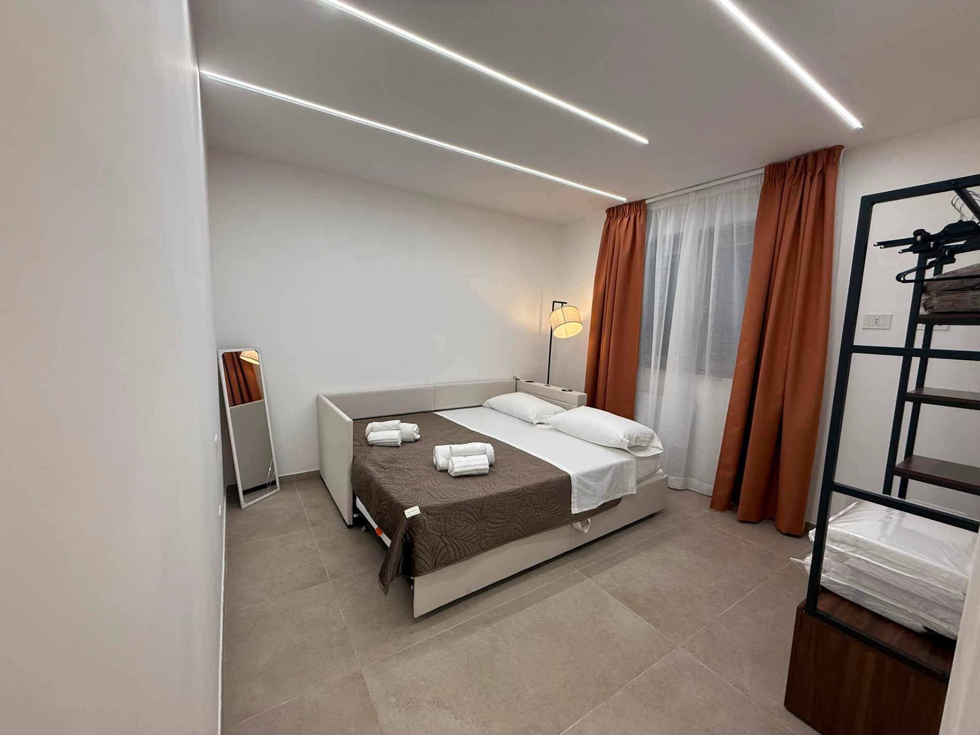 Camera con divano letto aperto, tende arancioni e LED a soffitto